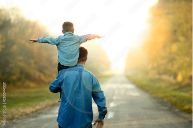 Father with son on shoulder holding arms out walking on country road into sunset