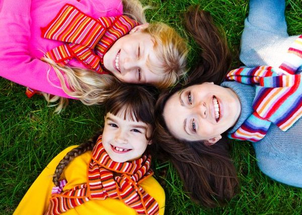 Mother and two girls broadly smiling in bright scarves lying on the grass
