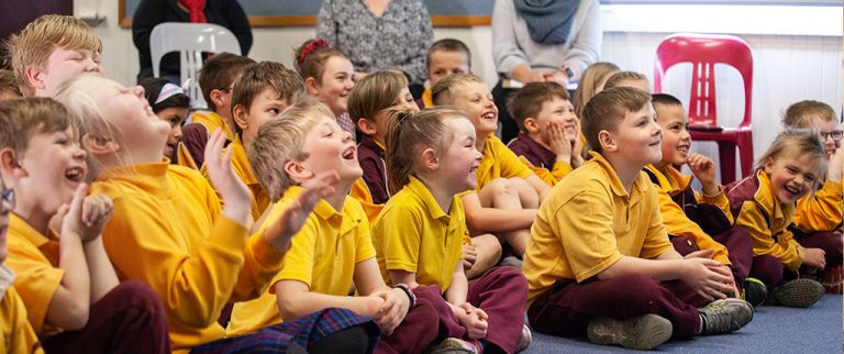 lower primary school children sitting on floor cross legged laughing and smiling