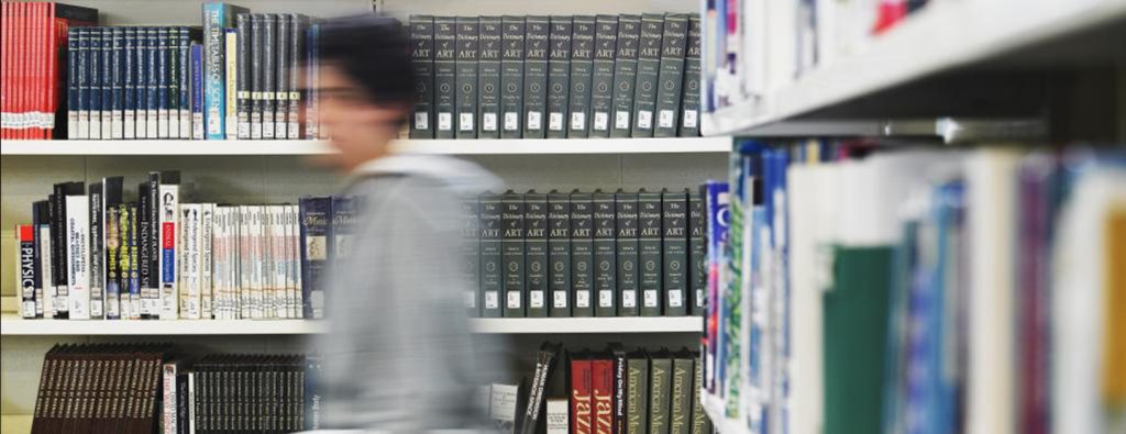 Bravehearts Research blurred man walking quickly in library in front of row of reference books