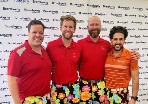 4 Golfers in front of Bravehearts Banner wearing flowery shorts and matching tops