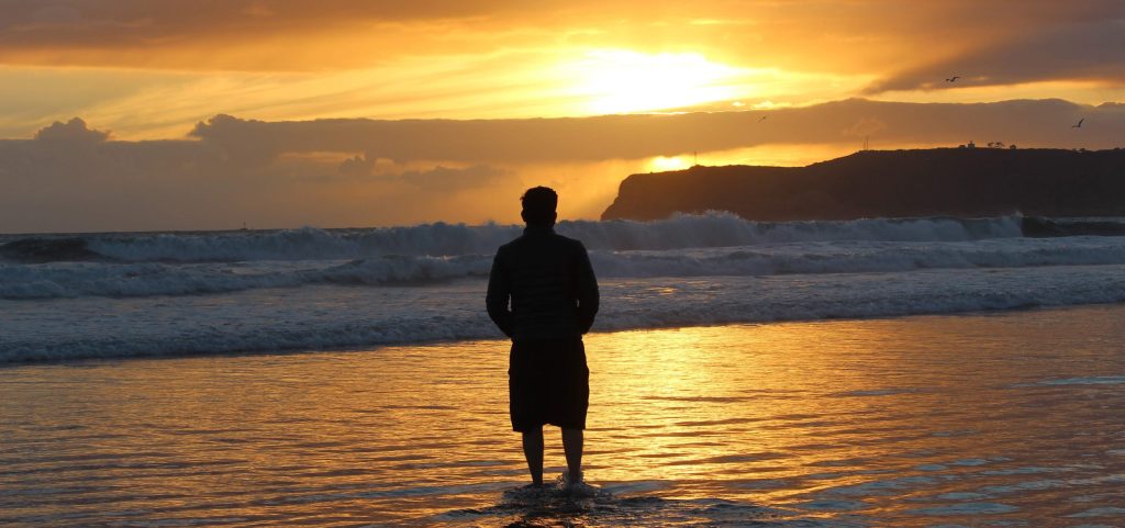 man standing on beach looking at the sunset